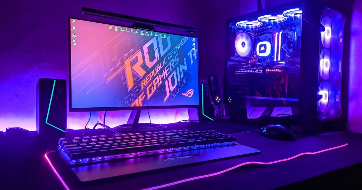 Budget Gaming PC Build: How to Split the Money, Not Which Parts to Buy A gaming PC with a glass side panel showing lit cooling fans, beside a monitor and an illuminated keyboard on a purple-lit desk