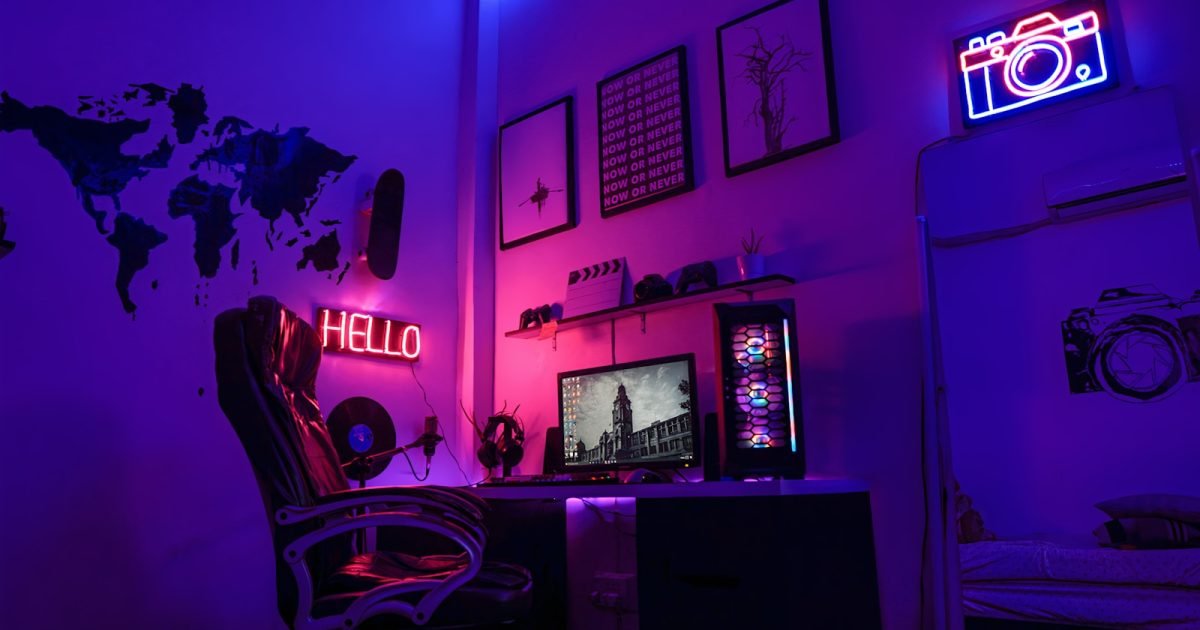 How to Build a White Gaming Setup Without Paying the Colour Tax A gaming room lit in purple and pink, with a racing-style chair, a corner desk, an RGB PC tower and neon signs on the wall